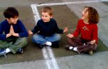 Children sitting in a playground with legs crossed and hands in prayer